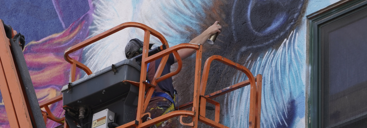 an artist painting a mural on a downtown Rock Island building in Arts Alley